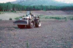 A landfill compacter being used to loosen and imprint the surface of an old gravel pit.