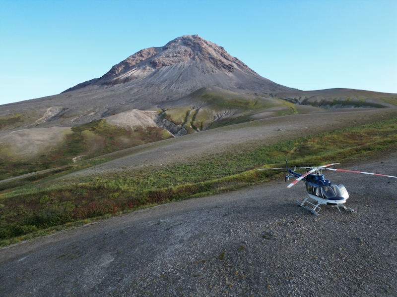 Wide photo of Augustine Island, with a helicopter in the foreground. 
          Photo by DMLW, decorative.