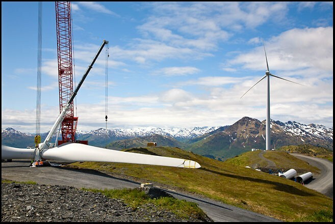 Parts of a turbine along a dirt road in the mountains, with a completed turbine back. 
          Photo by AK Renewables, decorative.