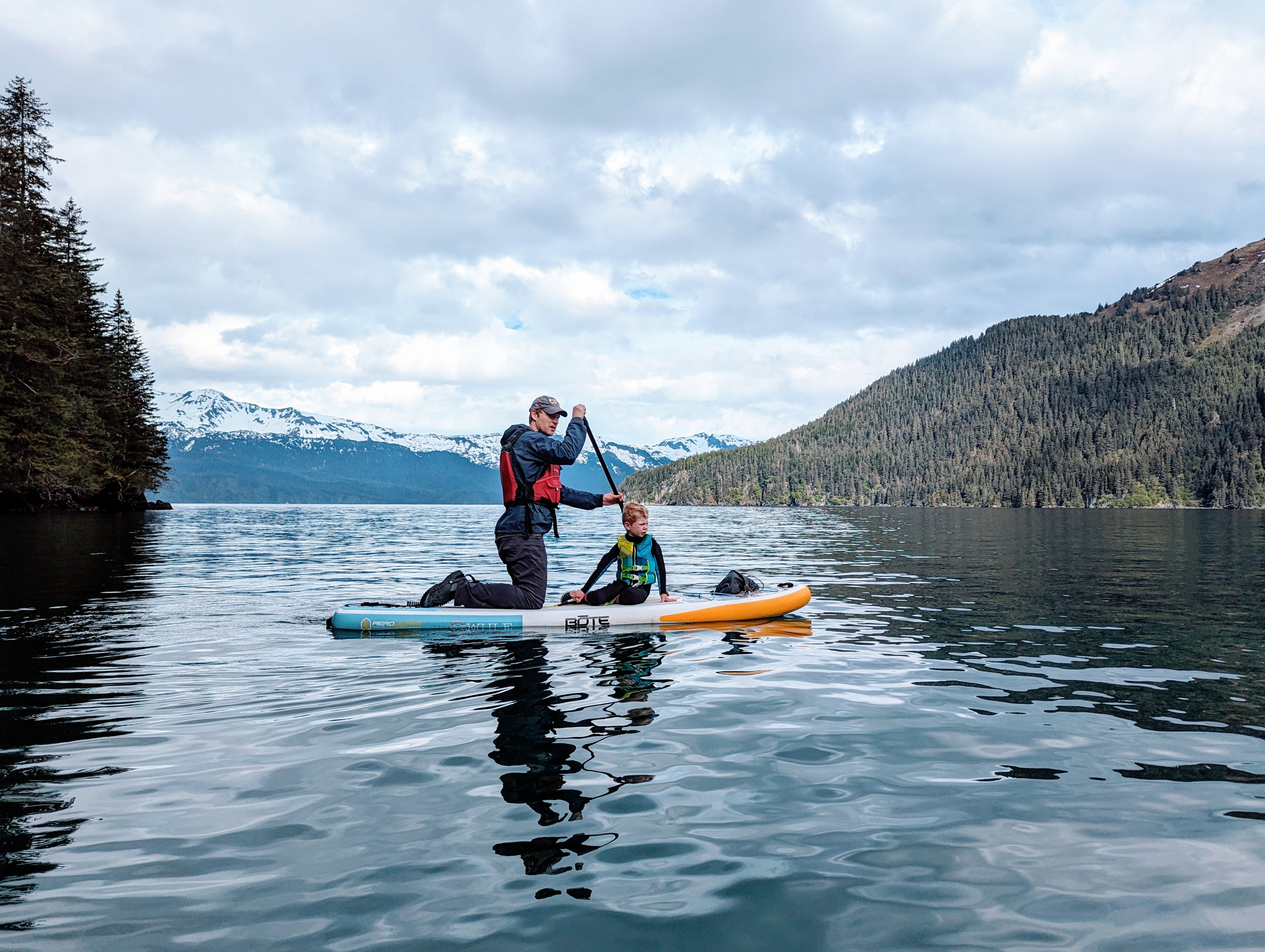 Father and young son Paddle Boarding wearing wet suits and life jackets