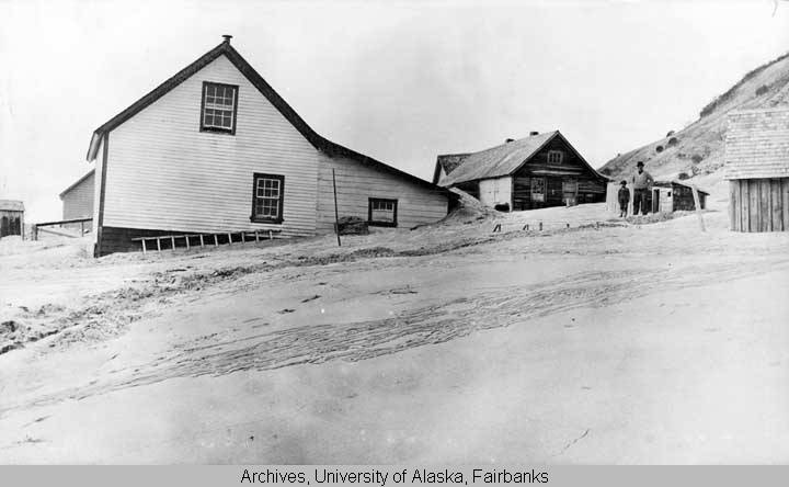 Ash covering buildings and the ground following the 1912 Katmai Eruption. A man and a child can be seen in the middle-right of the image, courtesy of University of Alaska Fairbanks, Alaska and Polar Re-gions Collections, Amelia Elkinton Collection, UAF-1974-175-398.