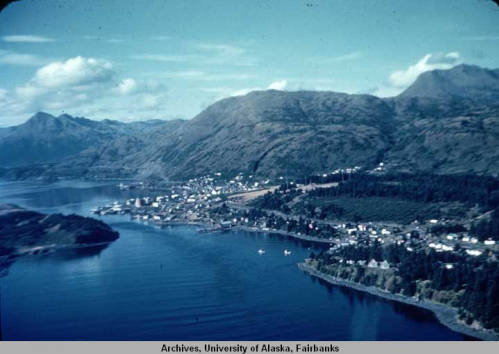 An arial view of Kodiak and the Woody Island Channel, taken circa 1949. Homes, roads, and two boats in a cove can be seen. Image courtesy of University of Alaska Fairbanks, Alaska and Polar Regions Collec-tions, George A. Morlander Photographs, UAF-1997-108-538.